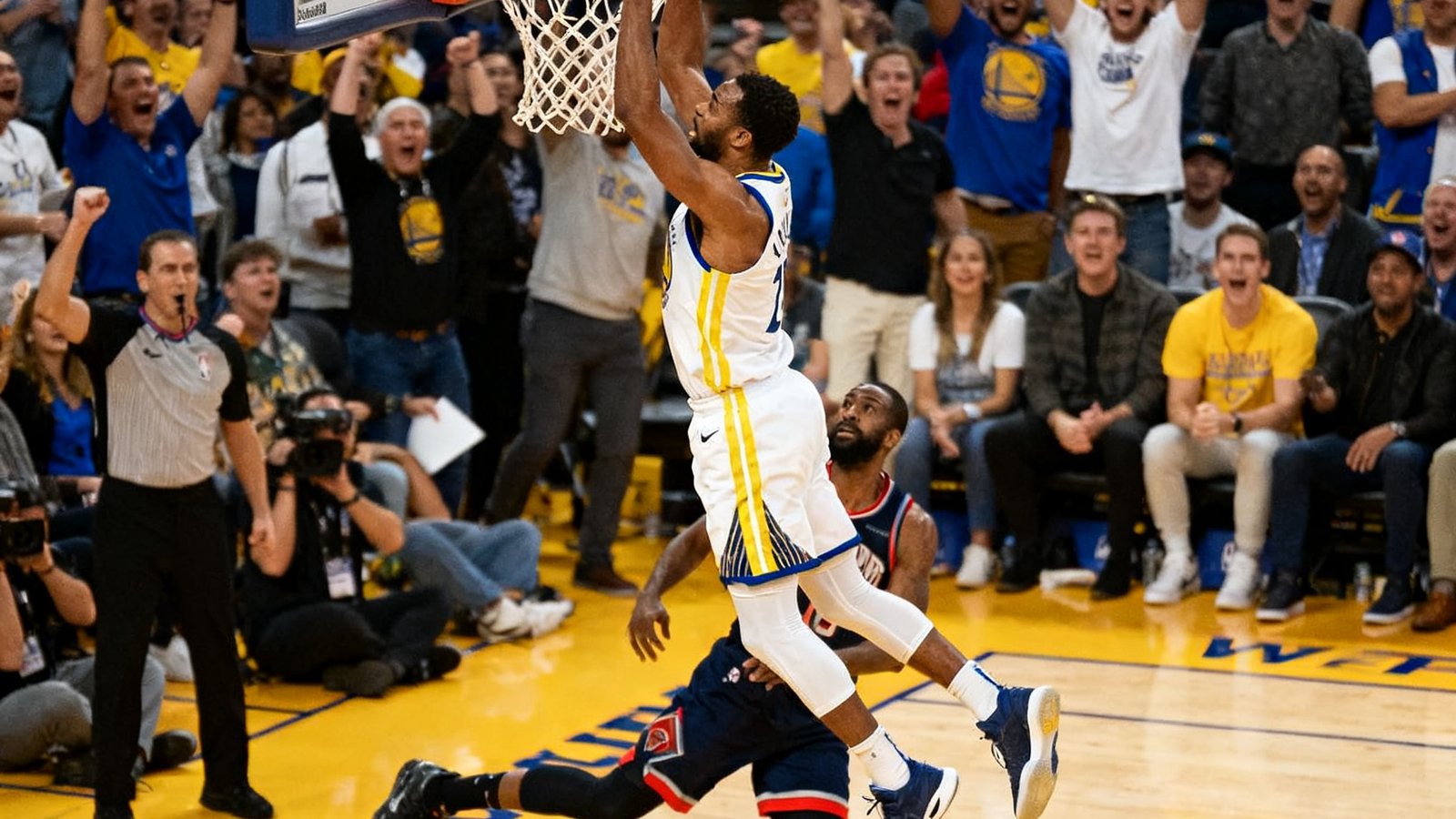 NBA常规赛中一名球员在快攻中完成单手劈扣，篮筐下的对手防守球员被弹开，现场观众全部起立欢呼